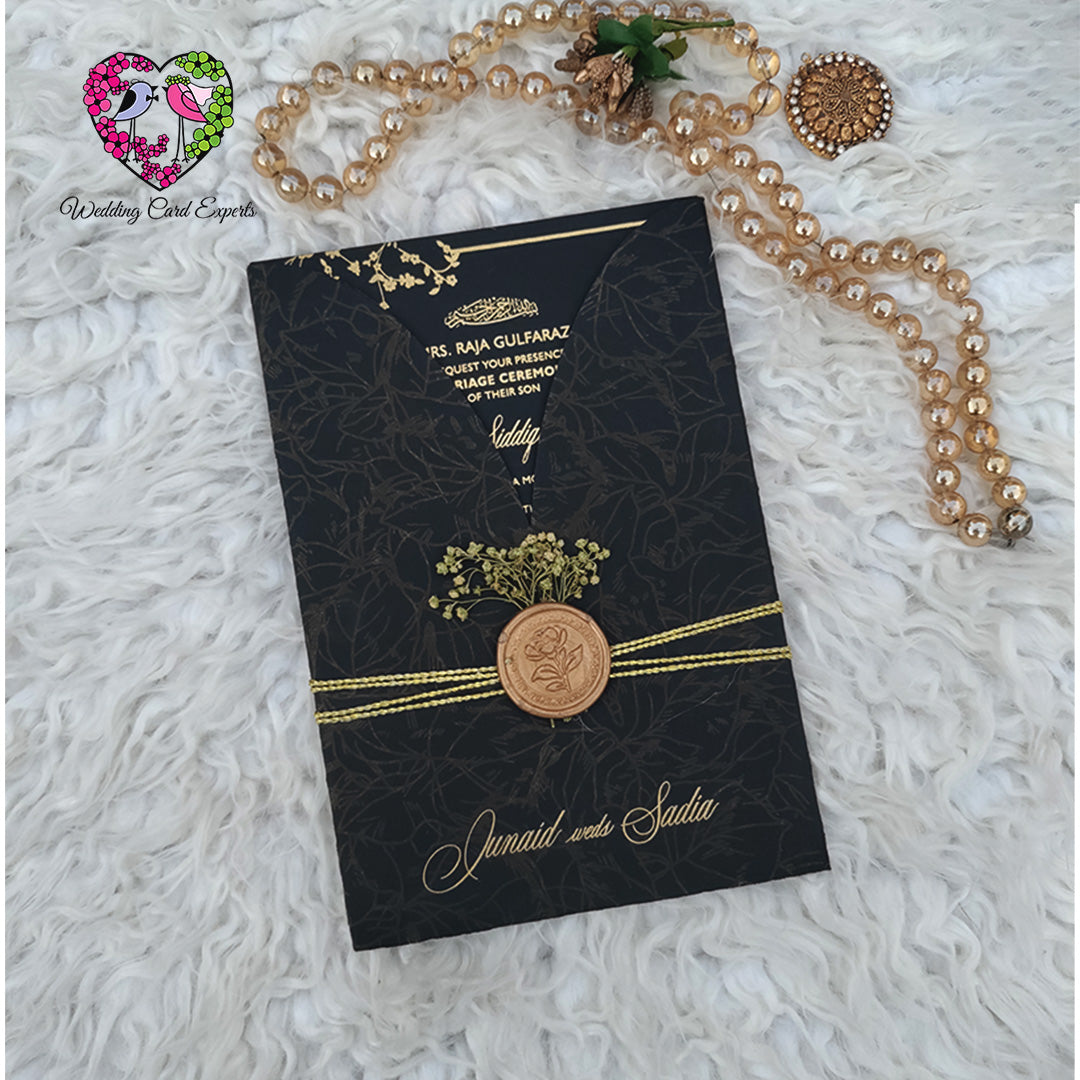 Wedding card design Pakistan — full black invitation card with gold botanical border frame and white gold typography beside matte black botanical folder, Pakistani wedding cards shipped to Berkshire UK