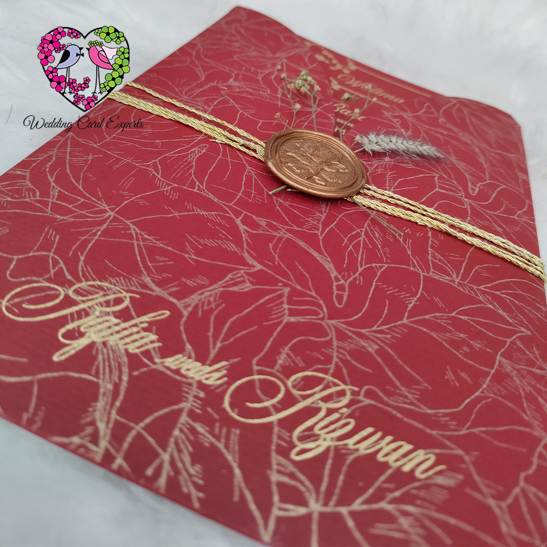 Pakistani wedding card close-up — gold foil botanical print crimson red envelope with copper wax seal and double gold twine wrap, wedding card Pakistan luxury