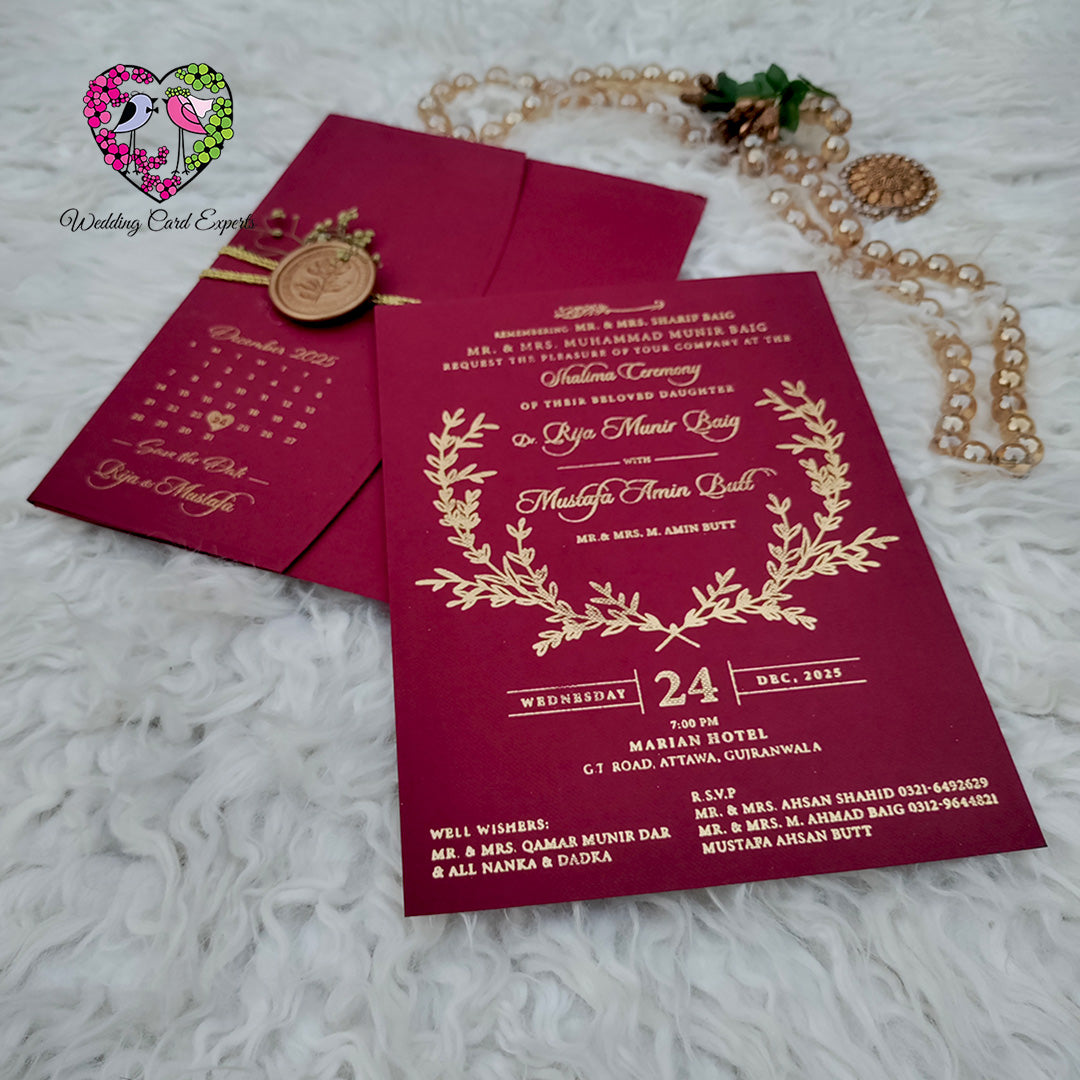 Luxury wedding cards Pakistan — burgundy textured folder with gold foil save the date calendar beside main invitation card with gold foil laurel wreath and botanical leaf detailing, wedding cards from Pakistan