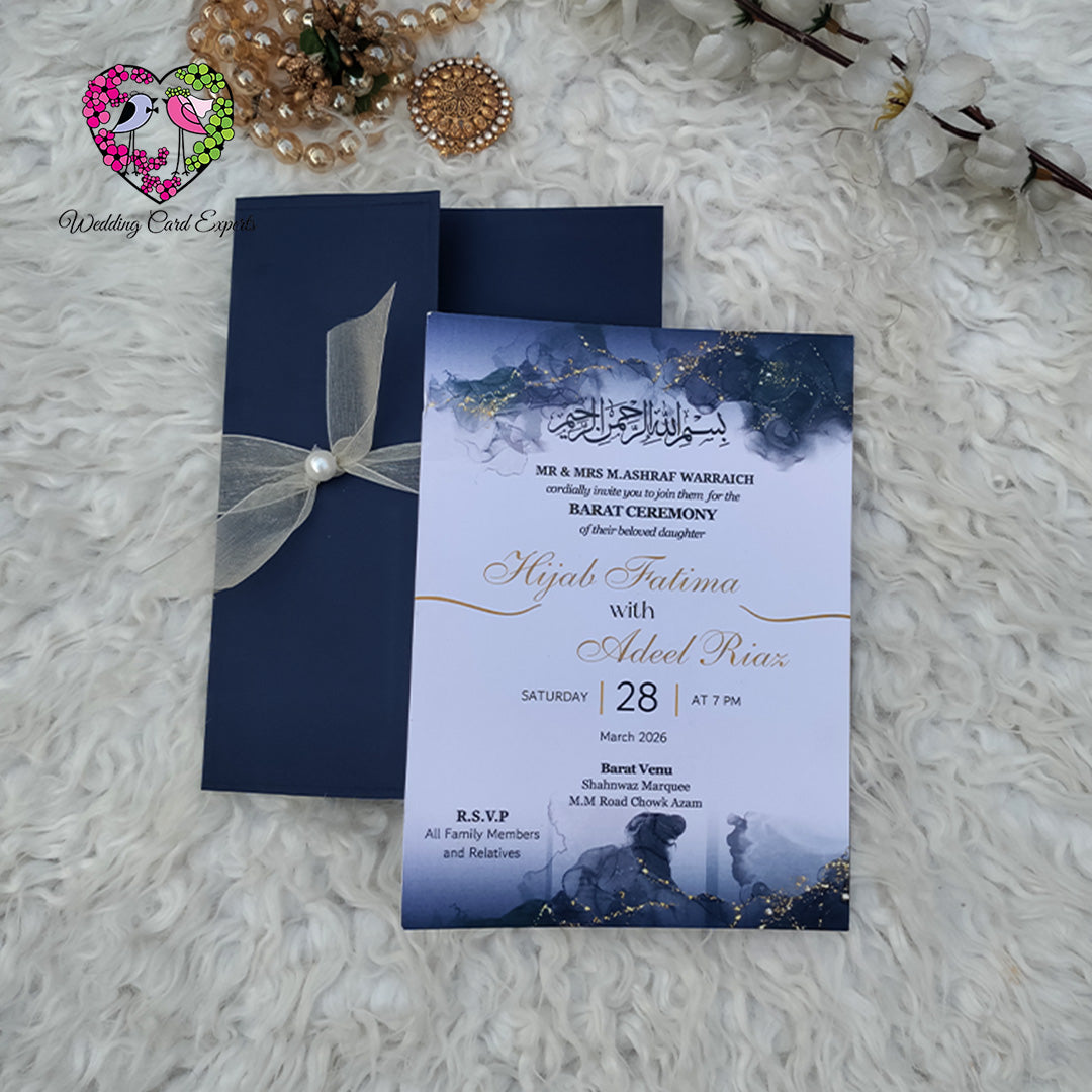 Pakistani wedding card — navy pocket folder tied with sheer ivory organza ribbon and pearl pin, watercolour barat invitation card peeking out, wedding cards from Pakistan